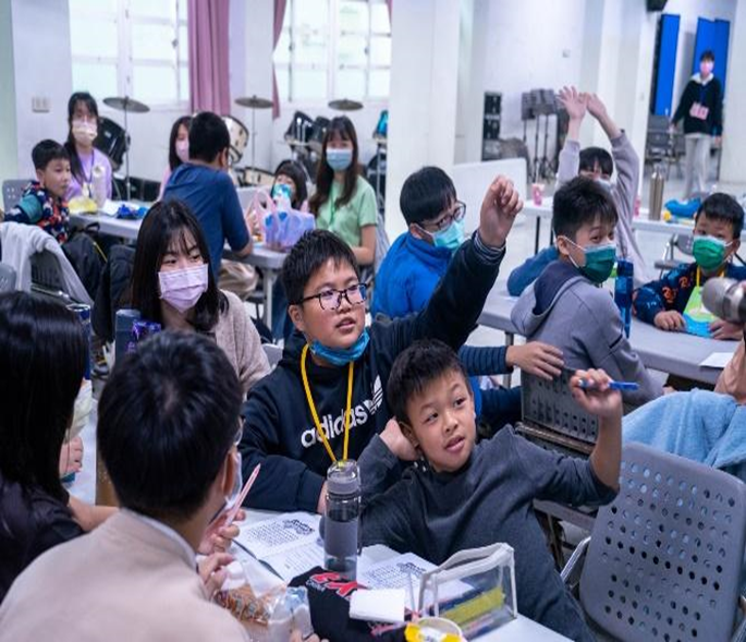 The Board Game Club interacting with children from Guosheng Elementary School. Through board games, the elementary school students learn through hands-on activities. The children enthusiastically raise their hands to answer questions and actively participate in the activities