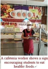 A cafeteria worker shows a sign encouraging students to eat healthy foods.